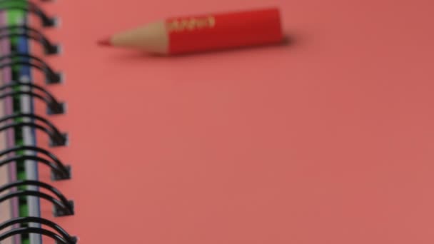 Un pequeño lápiz de madera rojo afilado aparece y se coloca en un bloc de notas rojo, video clip, primer plano - Metraje, vídeo