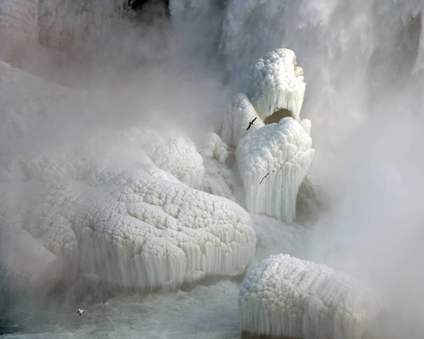 No inverno, a névoa das Cataratas do Niágara congela nas rochas abaixo, criando belas formações de gelo e esculturas. Gaivotas voam através da névoa na base das Cataratas. - Foto, Imagem