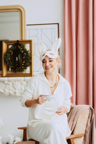 Gyönyörű, fiatal, boldog nő karneváli nyúl maszkban és fehér jelmezben, aki egy újat ünnepel egy modern karácsonyi enteriőrben. Inspiráció. Puha szelektív fókusz. - Fotó, kép