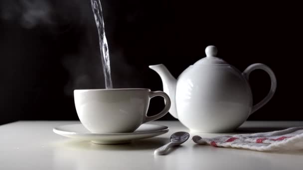 El agua caliente se vierte en una taza de té sobre una mesa blanca. - Metraje, vídeo