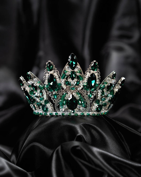 Korona dla Miss Piękności, symbol władzy i elegancji, rywalizacja, pokaz. Diadem w białym metalu i zielone kamienie na czarnym zasłoniętym satynowym tle - Zdjęcie, obraz
