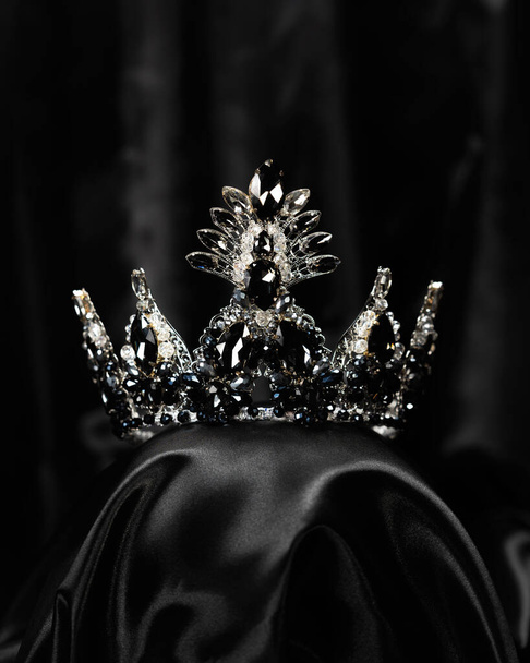 Corona para la señorita belleza, un símbolo de poder y elegancia, competencia, espectáculo. Diadema en metal blanco y piedras negras sobre fondo satinado negro - Foto, imagen