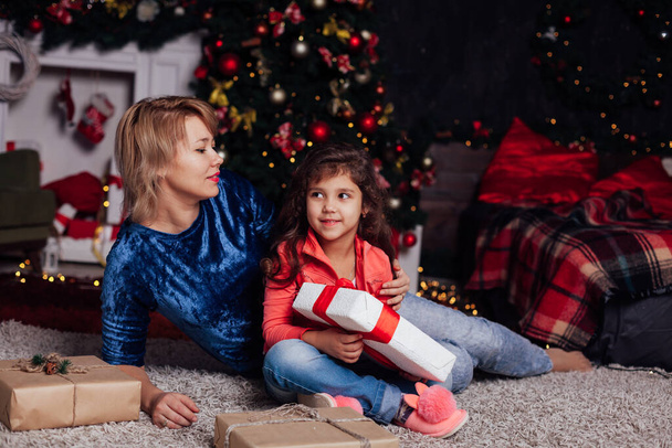 piccola ragazza riccia e madre all'albero di Natale con regali nuovo anno luci ghirlanda - Foto, immagini