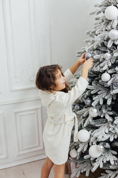 piccola ragazza riccia decora l'albero di Natale con regali nuovo anno luci ghirlanda - Foto, immagini