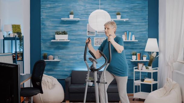 Mujer madura usando bicicleta estacionaria para hacer ejercicio físico - Foto, imagen