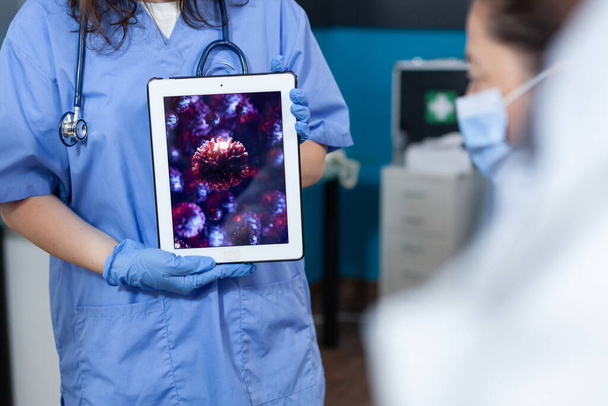 Nahaufnahme einer Krankenschwester, die einen Tablet-Computer mit Viren-Expertise in der Hand hält - Foto, Bild