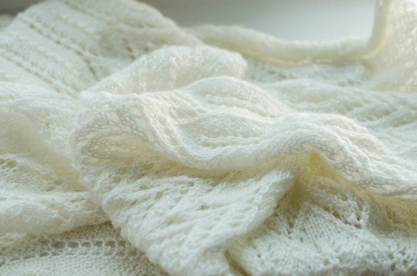 Knitted warm White scarf. Cozy composition in the home atrosphere. Wool fabric texture close up background. Comfortable style cloth. Wavy folds material. Soft focus - Photo, Image