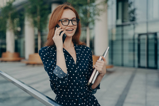 Iloinen punapää Eurooppalainen nainen puhuu nykyaikaisella matkapuhelimella on iloinen ilme - Valokuva, kuva