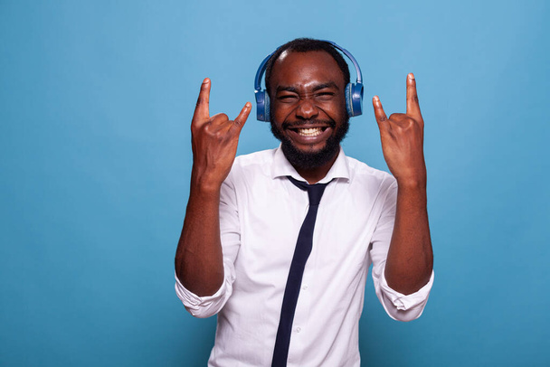 Smiling man full of energy doing rock and roll hand sign while listening to music - Zdjęcie, obraz