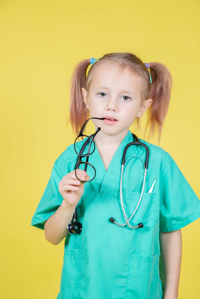 Portrait of serious little caucasian kid dressed in doctors green coat isolated on yellow - Φωτογραφία, εικόνα