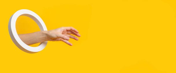 Mano con un foro rotondo raccoglie un oggetto invisibile su uno sfondo giallo. Bandiera - Foto, immagini