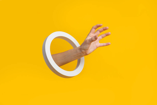 Χέρι με μια στρογγυλή τρύπα παίρνει ένα αόρατο αντικείμενο σε κίτρινο φόντο  - Φωτογραφία, εικόνα