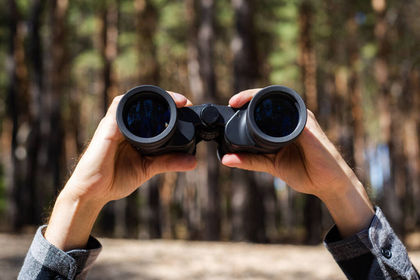 Man holds binoculars against the background of the forest. - Fotoğraf, Görsel