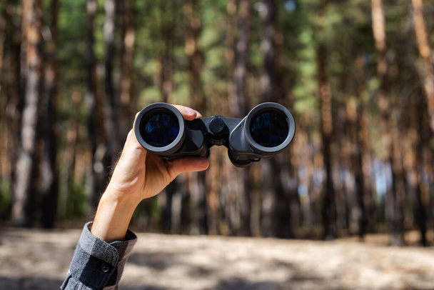 Male hand hold binoculars on the background of the forest. Banner. Flat lay, top view. - Photo, Image