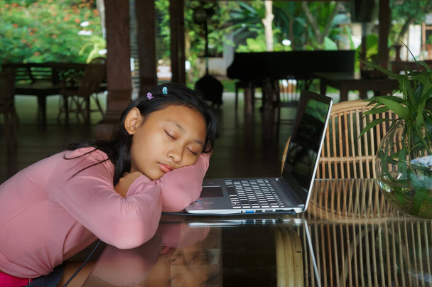 東南アジアの10代の少女は、オンライン教室の会議をしながら眠く感じる。彼女のラップトップと友達になるだけだ - 写真・画像
