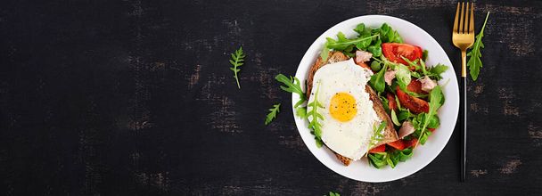 Breakfast - toast with fried eggs and tomatoes salad with greens and cod liver on dark background. Healthy breakfast. Top view, banner - Photo, Image