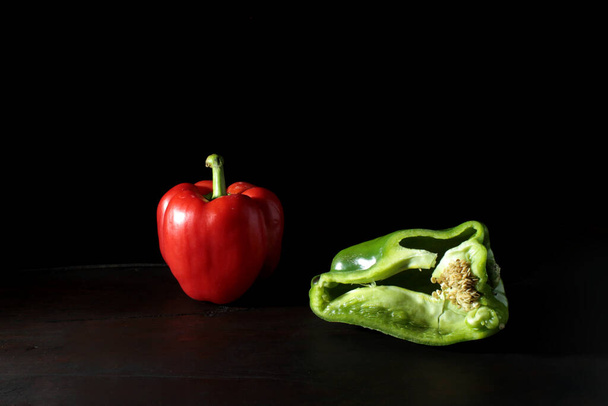 A red pepper and half green pepper on a dark wooden table and black background - Valokuva, kuva