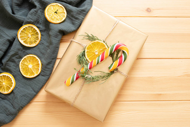Christmas wrapped gift in eco style. Golden gift box with Christmas tree, dry orange slice and traditional candy cane. Top view. Festive mood, gift wrapping idea concept. DIY - Photo, Image