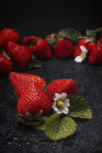 A vertical shot of strawberries on a natural slate base on the dark background - 写真・画像