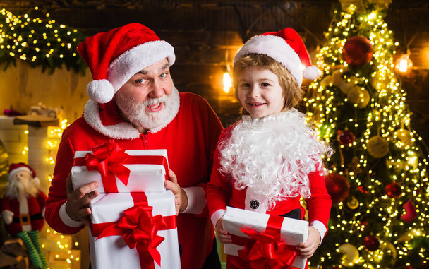 Santa Claus y pequeño ayudante con regalo de Navidad. Un regalo de año nuevo. Feliz infancia. Fondo de Navidad. - Foto, imagen