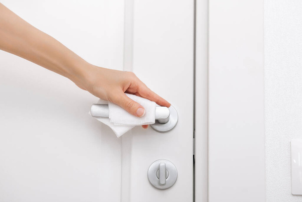 Cleaning door handles with an antiseptic wet wipe and gloves. Sanitize surfaces prevention in hospital and public spaces against corona virus. Woman hand using towel for cleaning home room door link - 写真・画像