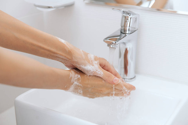 Washing hands under the flowing water tap. Hygiene concept hand detail. Washing hands rubbing with soap for corona virus prevention, hygiene to stop spreading corona virus in or public wash room - Zdjęcie, obraz