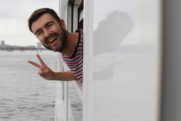 κοντινό πορτραίτο ενός όμορφου νεαρού άνδρα που κοιτάζει έξω από το παράθυρο του πλοίου ενώ ταξιδεύει  - Φωτογραφία, εικόνα