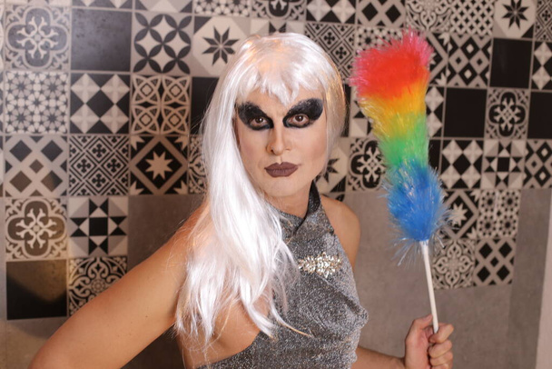 close-up portrait of transgender woman in wig and dress colorful feather duster at home - Photo, Image