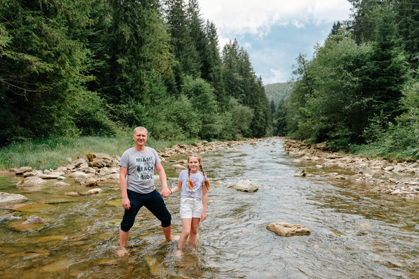 Children with father hiking in Alps mountains crossing river. Kids play in water at mountain. Spring family vacation. Little girl with dad on hike trail. Outdoor fun. Active recreation with children - 写真・画像