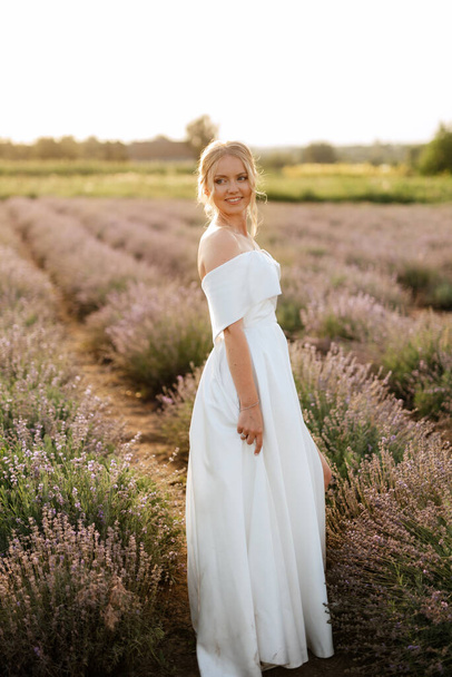 the bride in a white dress walks on the lavender field - Foto, afbeelding