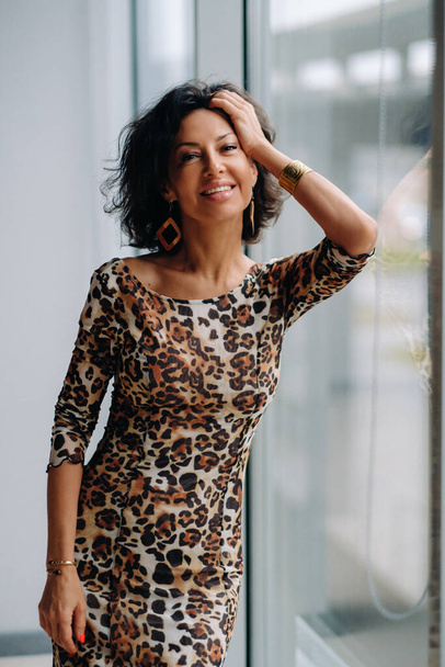 a brunette woman in a tiger dress stands near a large window. - Fotografie, Obrázek