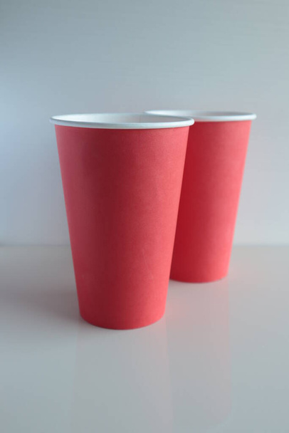 Červený papír jednorázové poháry stojí na lehkém povrchu. - Fotografie, Obrázek