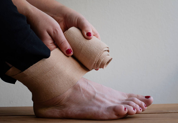 Frau wickelt elastischen Verband um verletzten Fuß, einen verstauchten Knöchel.  - Foto, Bild