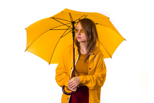 黄色のレインコートと眼鏡の少女が傘の下に立っている。白地に隔離. - 写真・画像
