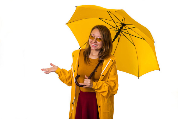 A smiling girl in a yellow raincoat stands under an umbrella and stretches out her hand in the rain. Isolate on white background. - 写真・画像