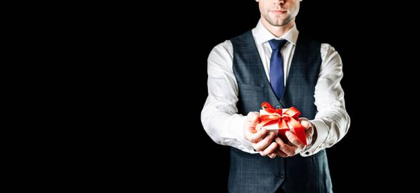 Gift man. Happy young businessman holding surprise gift box present with red ribbon isolated on black background. Black Friday, Valentine Day congratulations banner. - Photo, Image