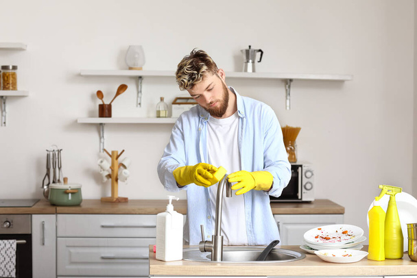 Jóképű fiatalember szivacs tisztító mosogató csap a konyhában - Fotó, kép