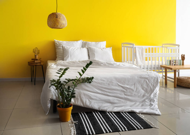 Nagy kényelmes ágy fehér bölcsővel közel sárga fal a szobában - Fotó, kép