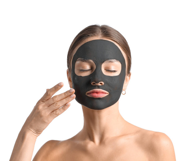 Mujer joven con máscara de carbón activado en su cara contra fondo blanco - Foto, Imagen