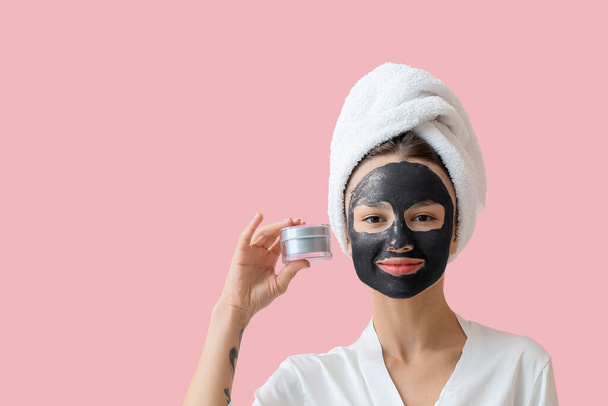 Jonge vrouw met geactiveerde houtskool masker op haar gezicht tegen kleur achtergrond - Foto, afbeelding