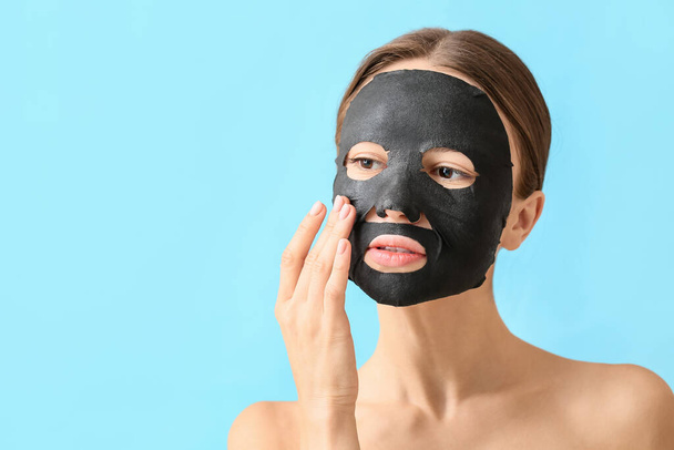 Mujer joven con máscara de carbón activado en su cara contra el fondo de color - Foto, imagen