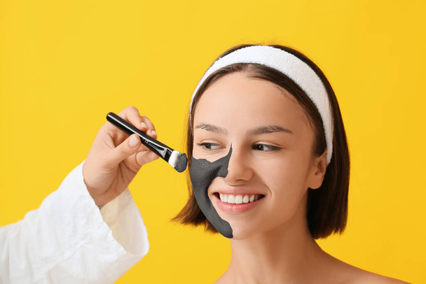 Cosmetólogo aplicando mascarilla de carbón activado en la cara de la mujer contra el fondo de color - Foto, imagen
