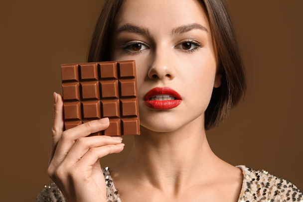 Beautiful woman with sweet chocolate on color background - Photo, Image