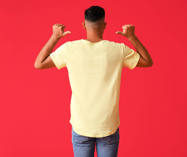 Hombre joven guapo en elegante camiseta sobre fondo de color, vista trasera - Foto, imagen