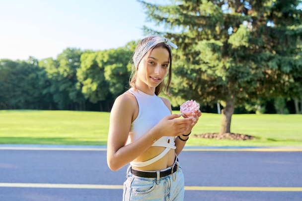 Portrait of cheerful teenage girl with donut cake, in summer park - 写真・画像