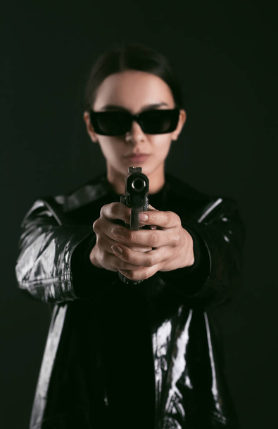 暗い背景の上にマトリックススタイルの銃を身に着けている女性 - 写真・画像