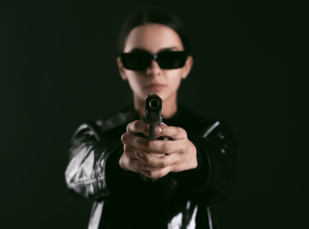 Siyah arka planda matris tarzı giyinmiş silahlı bir kadın. - Fotoğraf, Görsel