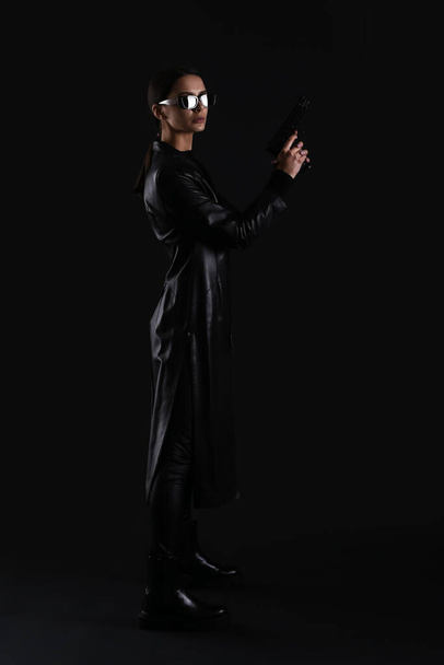 Woman with gun dressed in matrix style on dark background - Fotó, kép