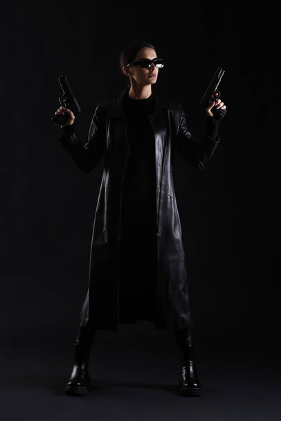 Woman with guns dressed in matrix style on dark background - Photo, Image