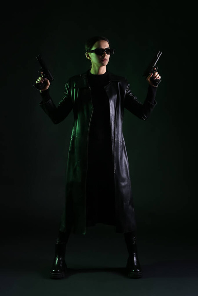 Woman with guns dressed in matrix style on dark background - Foto, Imagen